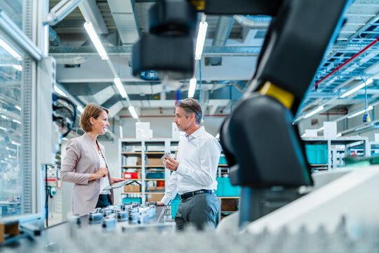 Two professionals discussing in a production hall with industrial robots - Powered by Adobe