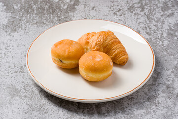Mini berliner or German donuts and croissant on white plate on stone table