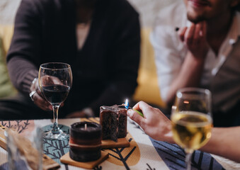 Friends gather around a table, sharing drinks and lighting a candle for ambiance. The scene conveys warmth, and togetherness, ideal for highlighting social gatherings or cozy indoor activities.