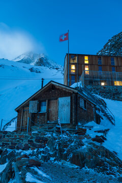 Finsteraarhorn Hut and Swiss flag at dusk below snow-covered mountains