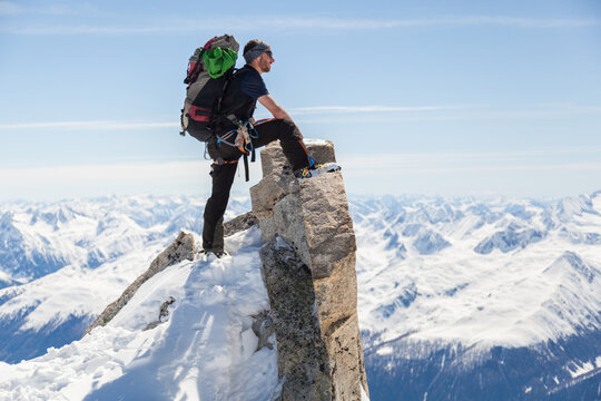 Man with pack and ski boots admires mountain view from rocky summit