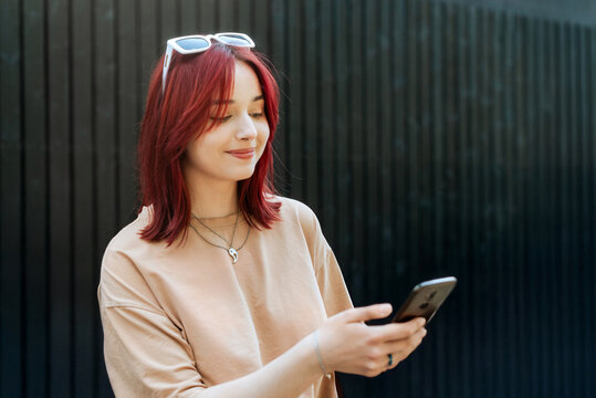 Young woman with red hair smiling and using smartphone