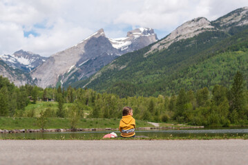 Child sits by lake in Fernie, British Columbia, with view of mountains