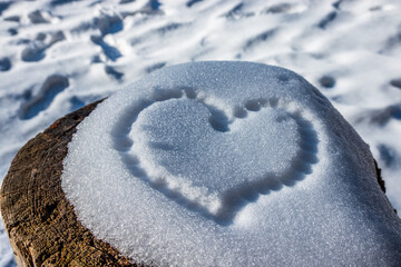 Heart shape carved into fresh snow on a log in a serene winter landscape, capturing the beauty of...