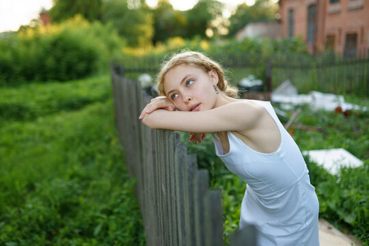 Girl in a white dress standing by a fence in a rural outdoor setting