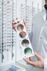 Male doctor in the optic shop holding a lens color scale in hands