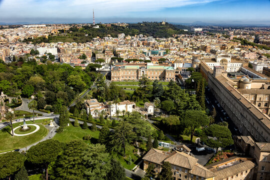 Lush green gardens and historical architecture stretch across a sprawling European cityscape under a clear blue sky. The panoramic view inspires travel to rich cultural heritage destinations.