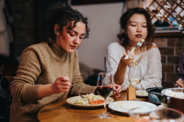 Two friends share a delicious and cozy dinner around a table. The overtones convey warmth, friendship, and quality time enjoying homemade food and conversation in an intimate setting.