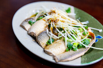 Overhead view of braised milkfish fillet on ceramic plate, garnished with shredded ginger and scallions, a chilled Taiwanese specialty