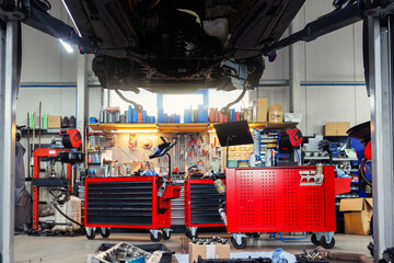 Scenic bottom POV disassembled SUV car with removed gearbox raised on lift elevator at workshop...