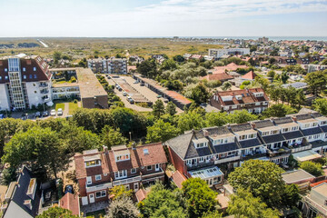 A scenic aerial shot captures the layout of a coastal village with homes, serene green areas, and roads leading toward the sea, showcasing urban and natural harmony.