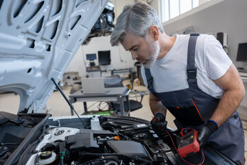 Fototapeta premium Man mechanic checking car battery using voltmeter in repair service