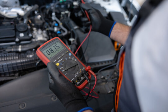 Repair specialist measuring battery charge with voltmeter for diagnostic service