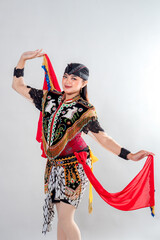 A Javanese female dancer in traditional Jathilan attire performs a graceful pose with red scarves,...