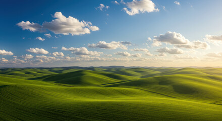 Obraz premium A stunning view of rolling green hills under a bright blue sky with fluffy white clouds.