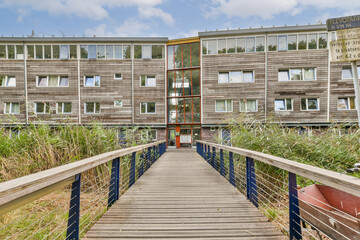 Fototapeta premium A contemporary wooden structure surrounded by greenery, featuring multiple windows and a walkway leading to its entrance, showcasing a blend of nature and architecture.