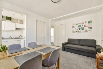 Fototapeta premium A stylish modern living room featuring minimalist furniture, a cozy dining area, plants, and vibrant wall art for an inviting atmosphere.