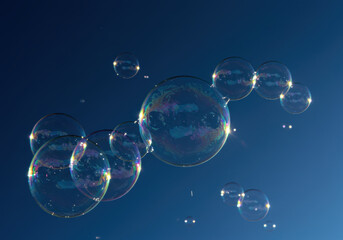 A collection of shimmering bubbles floats gently in the sky, with colorful reflections.