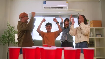 Happy asian diverse group friends playing together with beer pong at home office standing at the table enjoying time together. Office leisure and board games concept.