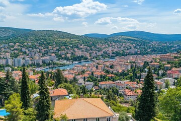 Fototapeta premium Panoramic view of a Mediterranean city nestled in a valley, showcasing a mix of residential buildings, a river or harbor, and lush greenery