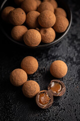 Chocolate truffles with cocoa powder and caramel filling on black table.