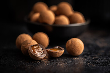 Chocolate truffles with cocoa powder and caramel filling on black table.