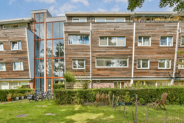 A contemporary wooden apartment building features multiple windows and greenery surrounding the structure. It showcases modern architecture in a residential area.