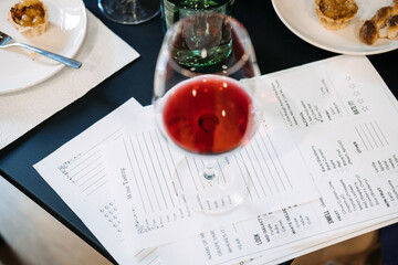 Glass of red wine resting on a wine tasting card at a workshop table with food pairings. Wine workshop, grape varietals, terroir exploration, wine knowledge experience