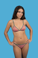 Fototapeta premium Confident model posing in pink and green bikini on blue backdrop