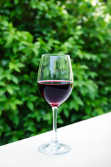 glass of rich red wine sits on a table against a vibrant green backdrop