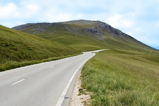 asphalt road winding through a green landscape towards a mountain