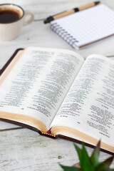 Obraz premium Open holy bible book with coffee cup and notebook on wooden desk. Christian Scripture study, biblical concept.