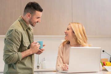Joyful couple engaging in meaningful conversation while enjoying coffee and sharing a delightful moment together in their cozy kitchen with a laptop open for their digital tasks and interactions