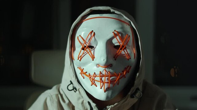 Masked figure in tech hoodie sits quietly with finger to lips, symbolizing digital protest, secret action or virtual resistance. Artistic expression of anonymous voice in online activism.