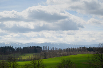 Rolling green hills and distant mountains under cloudy sky. Ideal for rural tourism, nature backgrounds, real estate brochures and landscape design visuals.