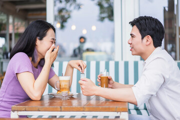 Couple enjoying drinks and laughter at a cozy cafe during a sunny afternoon