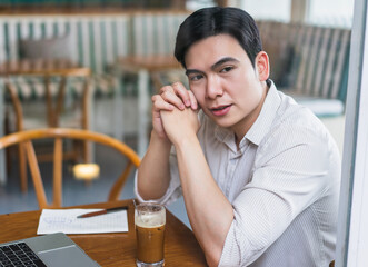 Friendly young man sitting at a cafe table with a drink, laptop, and notepad during a relaxed afternoon