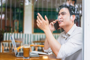 Young man enjoying coffee while talking on the phone and working on a laptop at a cafe