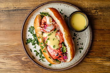 delicious lobster roll served on toasted bun, garnished with fresh herbs and accompanied by side of creamy sauce