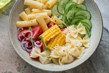 Pasta salad with farfalle, tortiglioni, cucumber, tomatoes and sweet corn in a beige plate,...