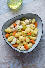 Bowl of vegetable soup with chicken and potato gnocchi, vertical shot on a blue and beige stone background, elevated view