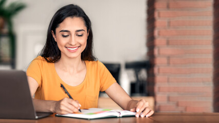 Smiling arab girl working online at cafe, making day plan, using laptop