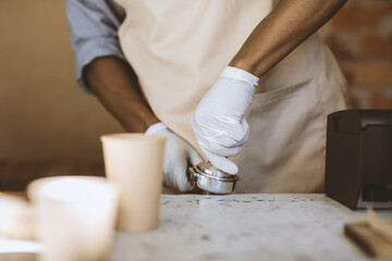 Great service and delicious coffee takeaway during social distance in modern cafe. Millennial african american barista in apron and gloves prepares espresso for client, cropped, close up, free space