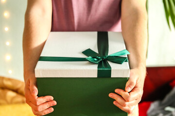 A man hand holding a green gift box with a ribbon, isolated on a neutral background. The...