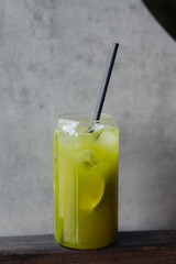 A refreshingly cool green iced drink with a black straw, set against a modern concrete background, perfect for summer hydration.
