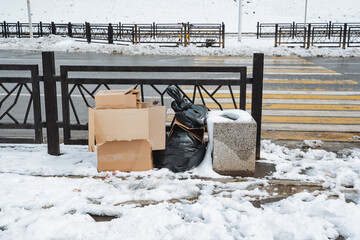 A large pile of trash is carelessly sitting in the cold snow next to a worndown fence, which...