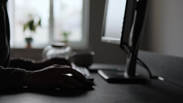 A man takes a break from working in home office. He puts down his glasses on the desk and pours himself a cup of tea. Close-up computer mouse and glasses. Freelance work and remote routine at home.