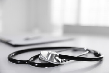 Stethoscope and paperwork on white desk in hospital, selective focus. Space for text