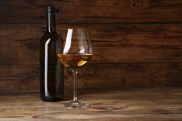 Tasty white wine in glass and bottle on wooden table, space for text