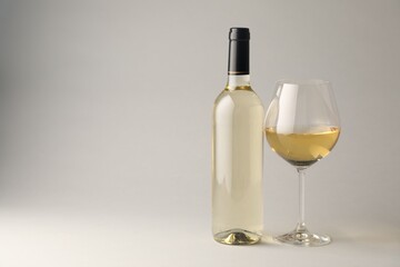 Tasty white wine in glass and bottle on light grey background, space for text